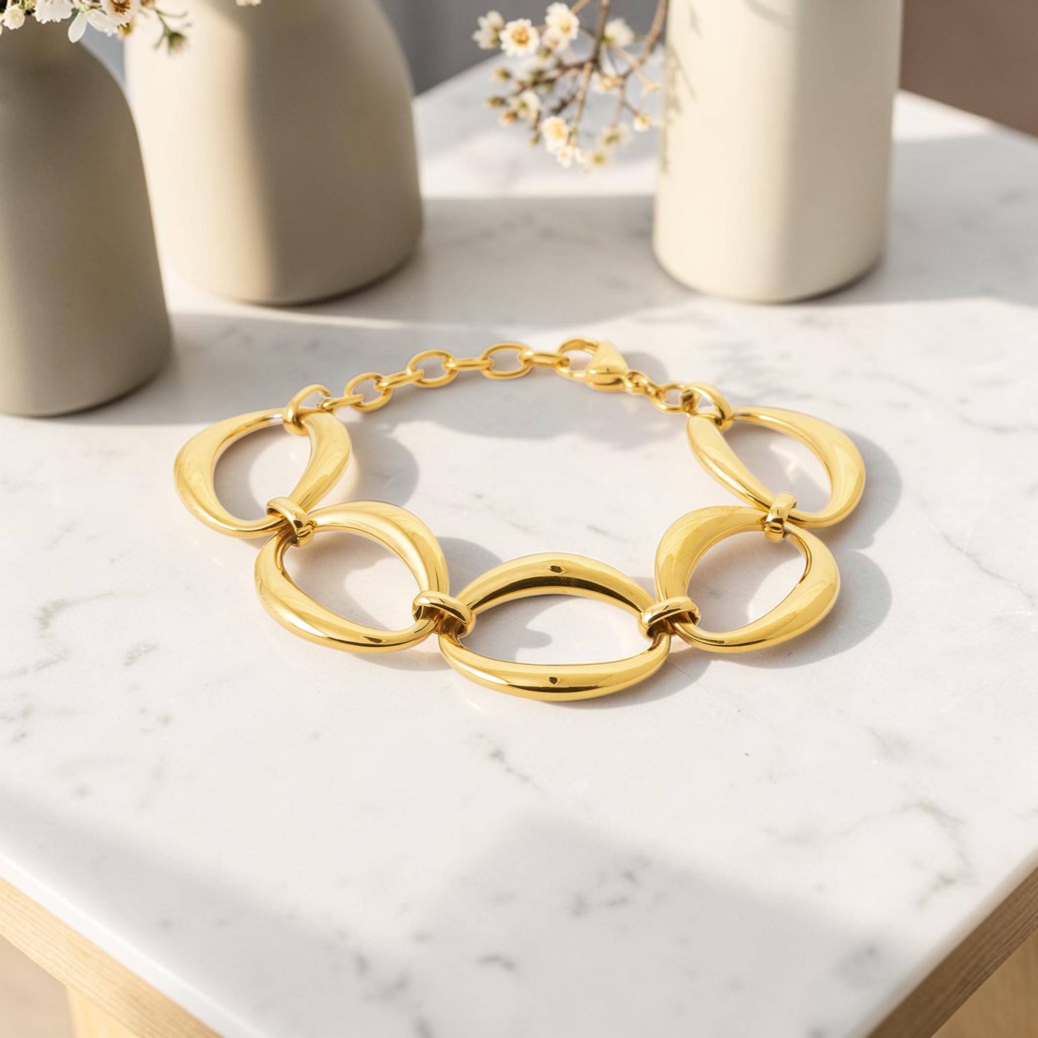 View of a Gold Oval Link Bracelet opened lay on a white marble table with flower vases
Material:  18K Gold Filled, stainless steel base
Color: yellow gold
Style: modern, elegant, statement, minimalist
Design details: large polished open oval links, smooth rounded profile, sculptural chain design, lobster clasp with extender
Best for: everyday elevated wear, statement styling, gifting, special occasions, modern jewelry lover