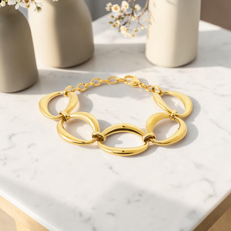 View of a Gold Oval Link Bracelet opened lay on a white marble table with flower vases
Material:  18K Gold Filled, stainless steel base
Color: yellow gold
Style: modern, elegant, statement, minimalist
Design details: large polished open oval links, smooth rounded profile, sculptural chain design, lobster clasp with extender
Best for: everyday elevated wear, statement styling, gifting, special occasions, modern jewelry lover