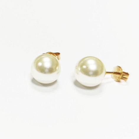 Une paire de boucles d'oreilles à clous en perles. Chaque boucle d'oreille présente une grosse perle ronde de couleur crème fixée sur une tige en or avec un fermoir papillon. Les boucles d'oreilles sont présentées sur une surface blanche.