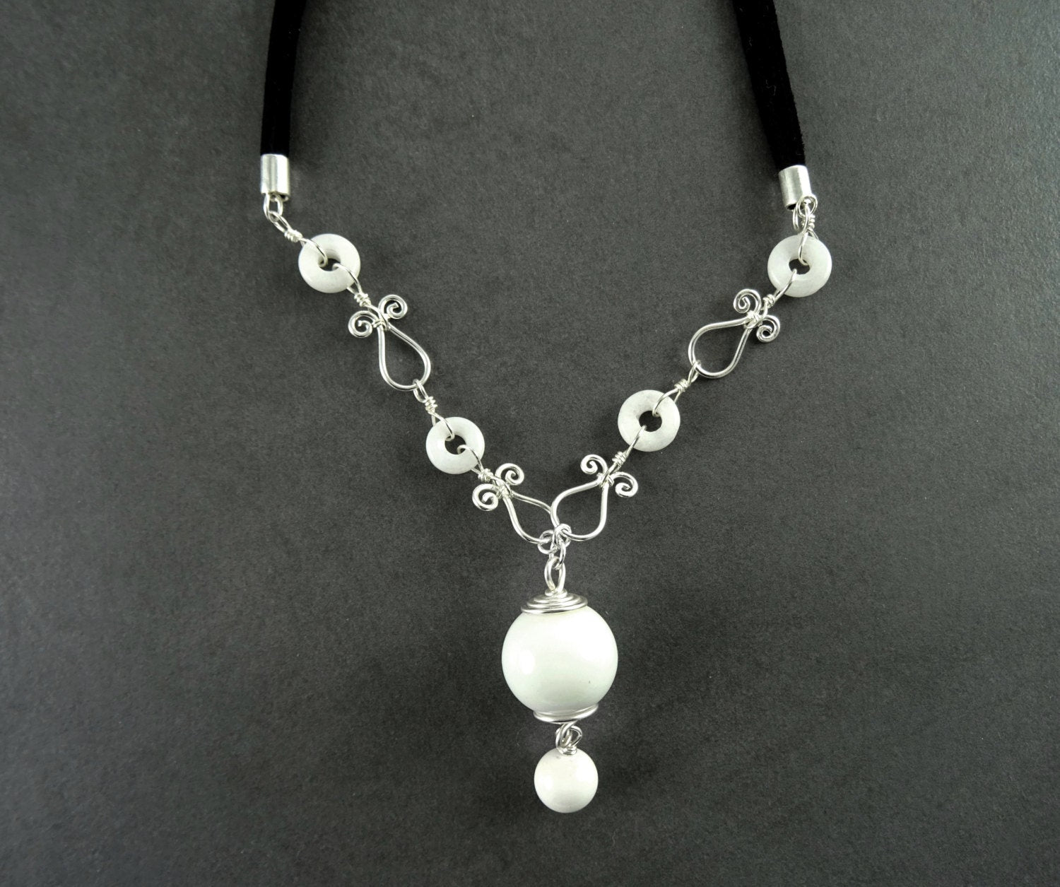 Peut inclure: Un collier blanc et argent avec un grand pendentif blanc et de petites perles blanches. Le collier est fait de fil et a un design délicat et féminin.