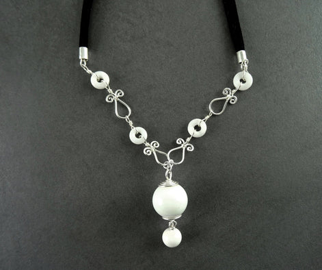 Peut inclure: Un collier blanc et argent avec un grand pendentif blanc et de petites perles blanches. Le collier est fait de fil et a un design délicat et féminin.