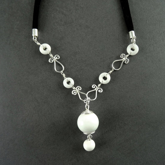 Peut inclure: Un collier blanc et argent avec un grand pendentif blanc et de petites perles blanches. Le collier est fait de fil et a un design délicat et féminin.