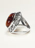 Peut inclure: Bague en argent ornée d'une pierre d'ambre ovale. La pierre d'ambre présente des couleurs chaudes et riches. L'anneau de la bague a un design ouvert avec des détails de filigrane décoratifs sur les côtés, ajoutant une touche élégante.