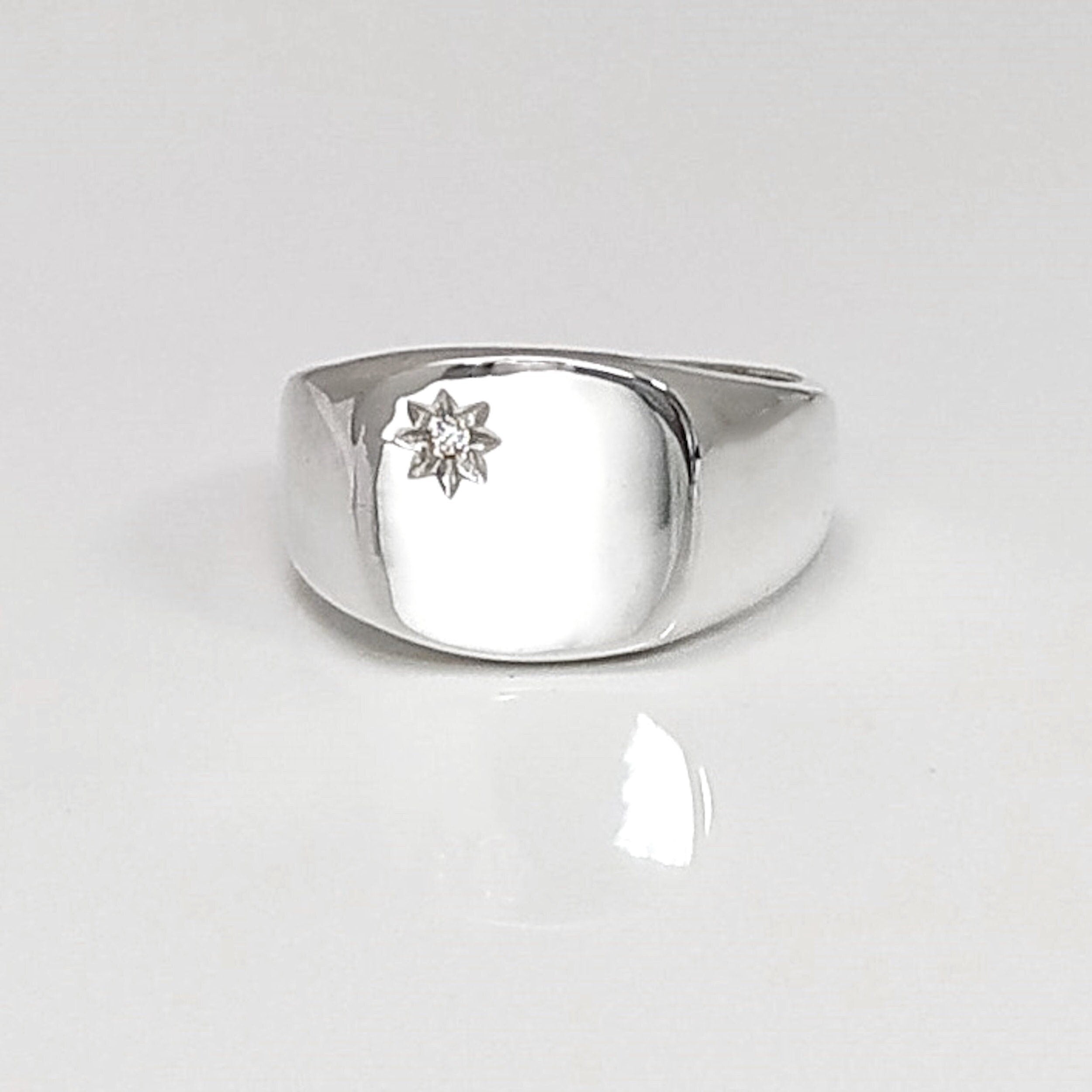 Peut inclure: Une bague signet en argent avec un petit diamant clair serti au centre en forme d'étoile.