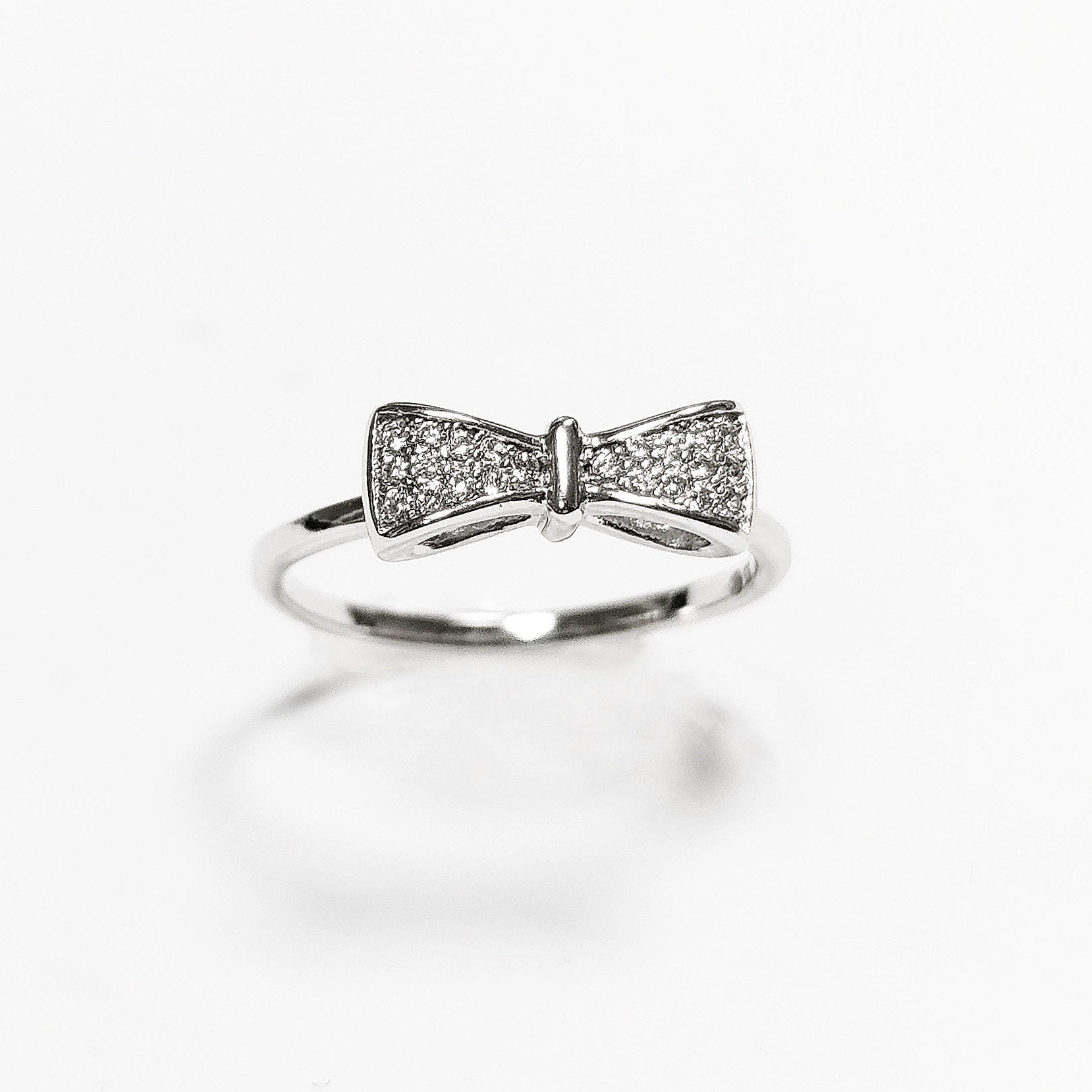 Peut inclure: Une bague en argent avec un motif en forme de nœud orné de petites pierres claires.