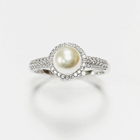 May include: A silver ring with a central, cream-coloured pearl surrounded by a halo of small, clear gemstones. The ring's band is also set with similar gemstones, creating a sparkling effect. The ring is displayed against a white background.