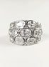 Peut inclure: Une large bague argentée ornée de plusieurs pierres précieuses ovales et transparentes. Les pierres sont disposées en couches, créant un design audacieux et scintillant. La bague est posée sur un fond blanc uni.