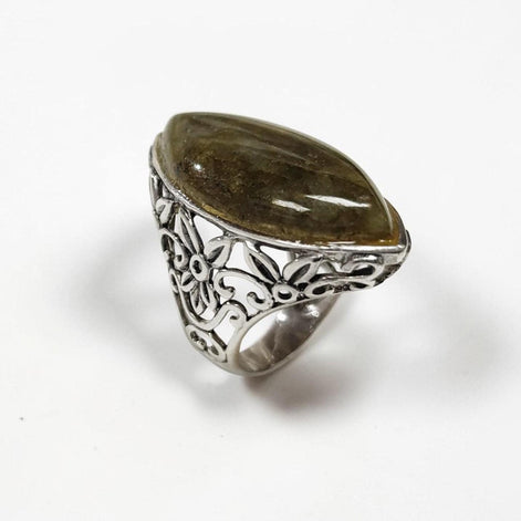 Peut inclure: Une bague en argent ornée d'une pierre ovale vert olive. La bague présente un motif floral ajouré sur le corps. La pierre est sertie dans un chaton en argent. La bague est présentée sur un fond blanc.