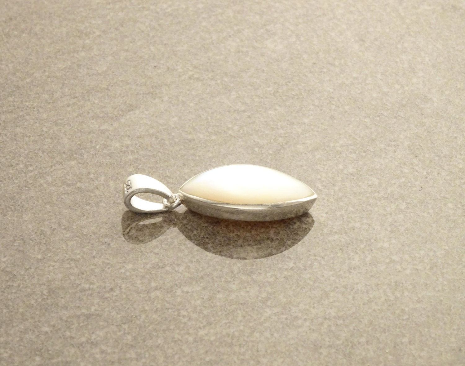 Un pendentif en argent avec une pierre ovale en nacre blanche. Un charm moderne fabriqué main par des créateurs reconnus, avec des éléments de qualité. Une boutique fiable pour un achat sécurisé.