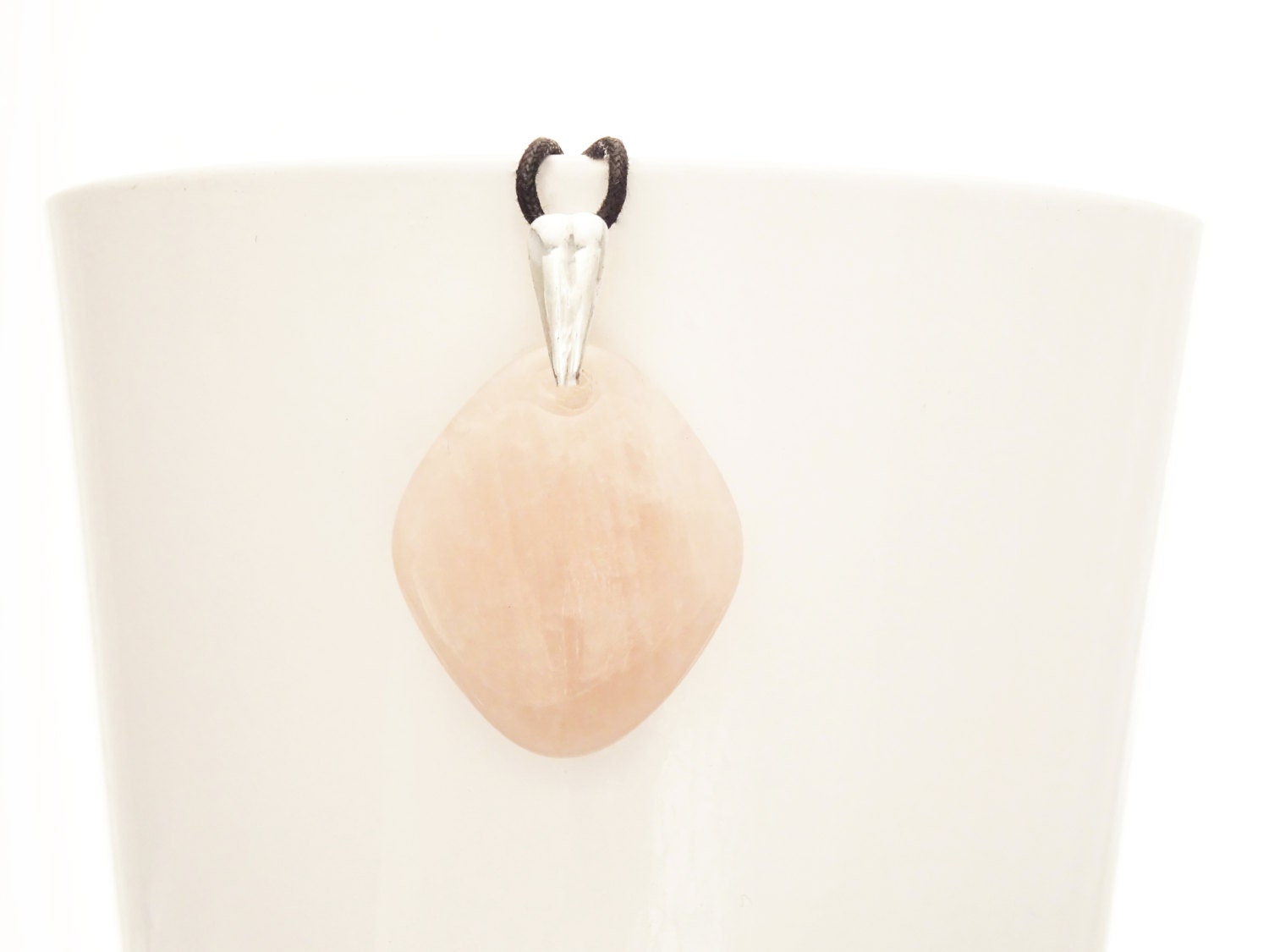 Un pendentif en pierre quartz rose avec une bélière en argent, 925 suspendu à un cordon noir.